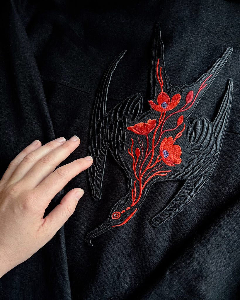 Black fabric with red floral embroidery on a frigate bird patch and a hand touching it