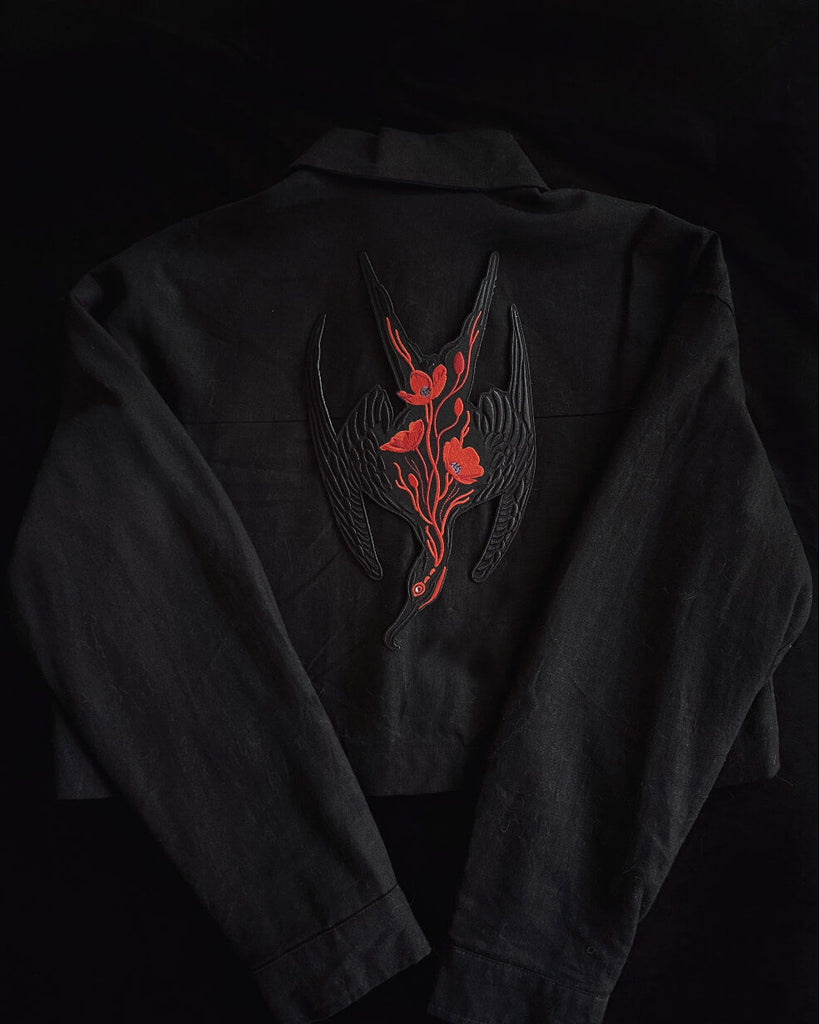 Black jacket with red and black floral embroidery frigate bird patch on a dark background