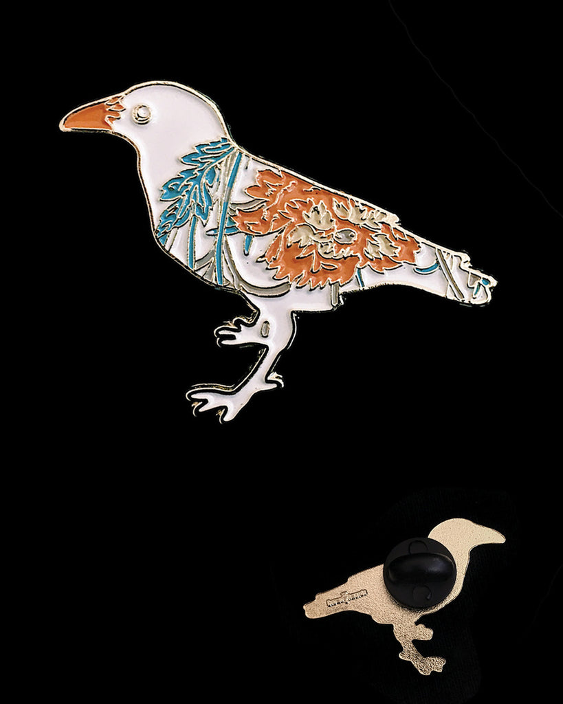 Small enamel pin of a white crow with orange and blue floral pattern.