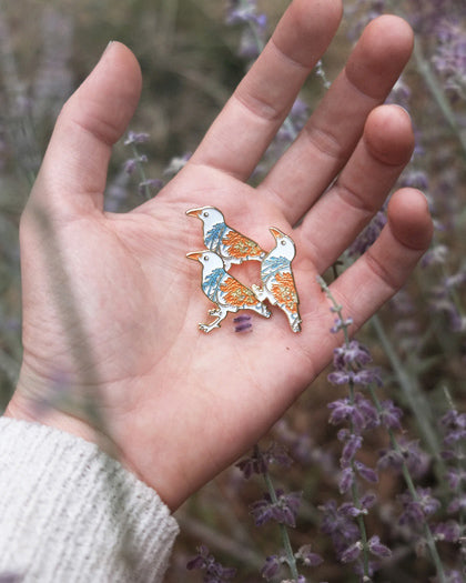 Small enamel pin of a white crow with orange and blue floral pattern.