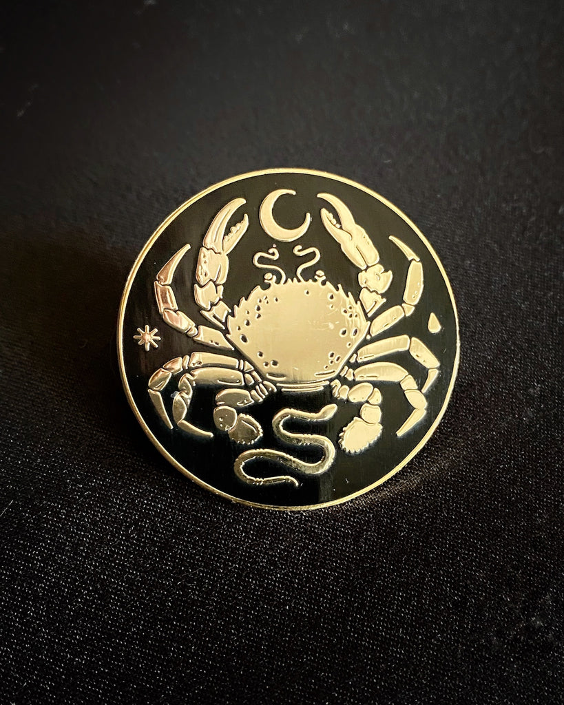 Small black enamel pin with gold-plated crab, moon, and snake design.