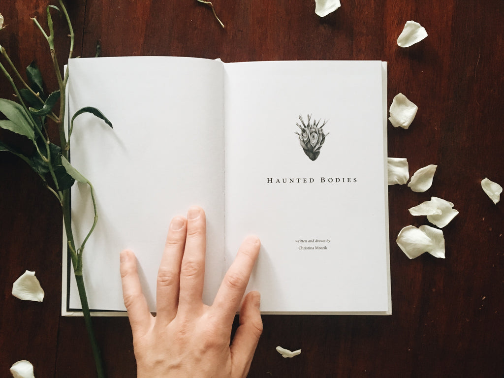 Small, hardback book with white linen cover and silver foil illustration of a flower with a bird claw for roots.