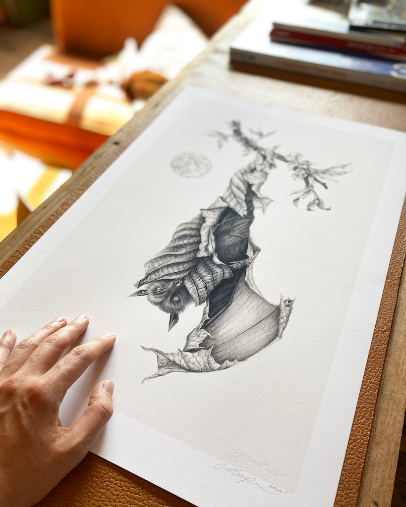 Art print of a graphite bat with leaves for wings, hanging upside down next to a full moon.