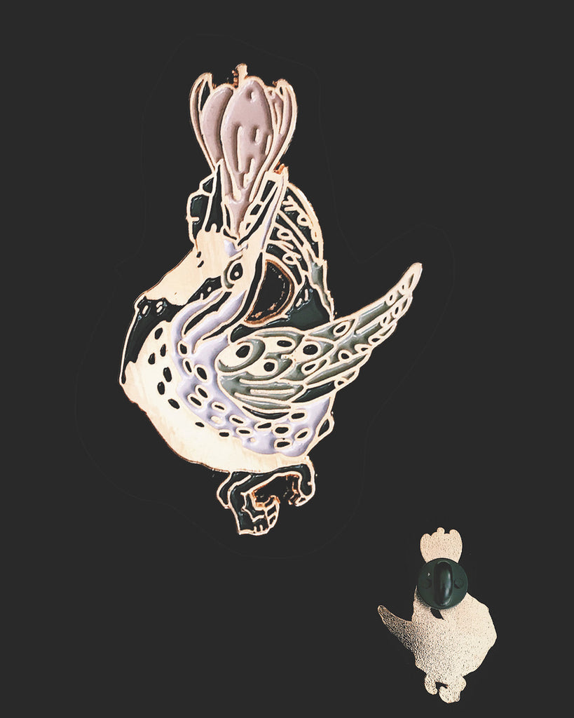 Small enamel pin of a black and white meadowlark with a pink flower growing from its open beak.